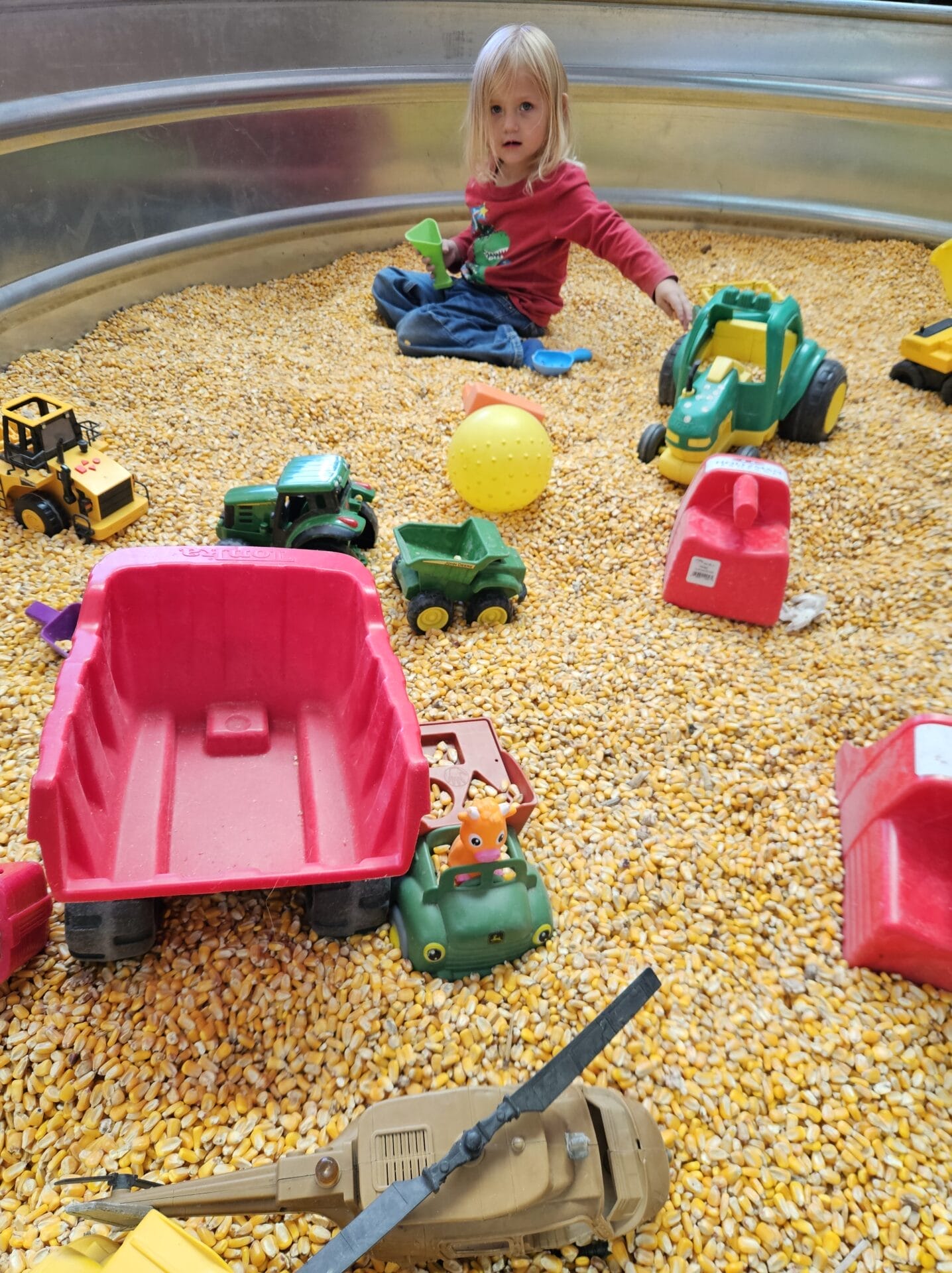 Child playing with toy trucks in corn bin
